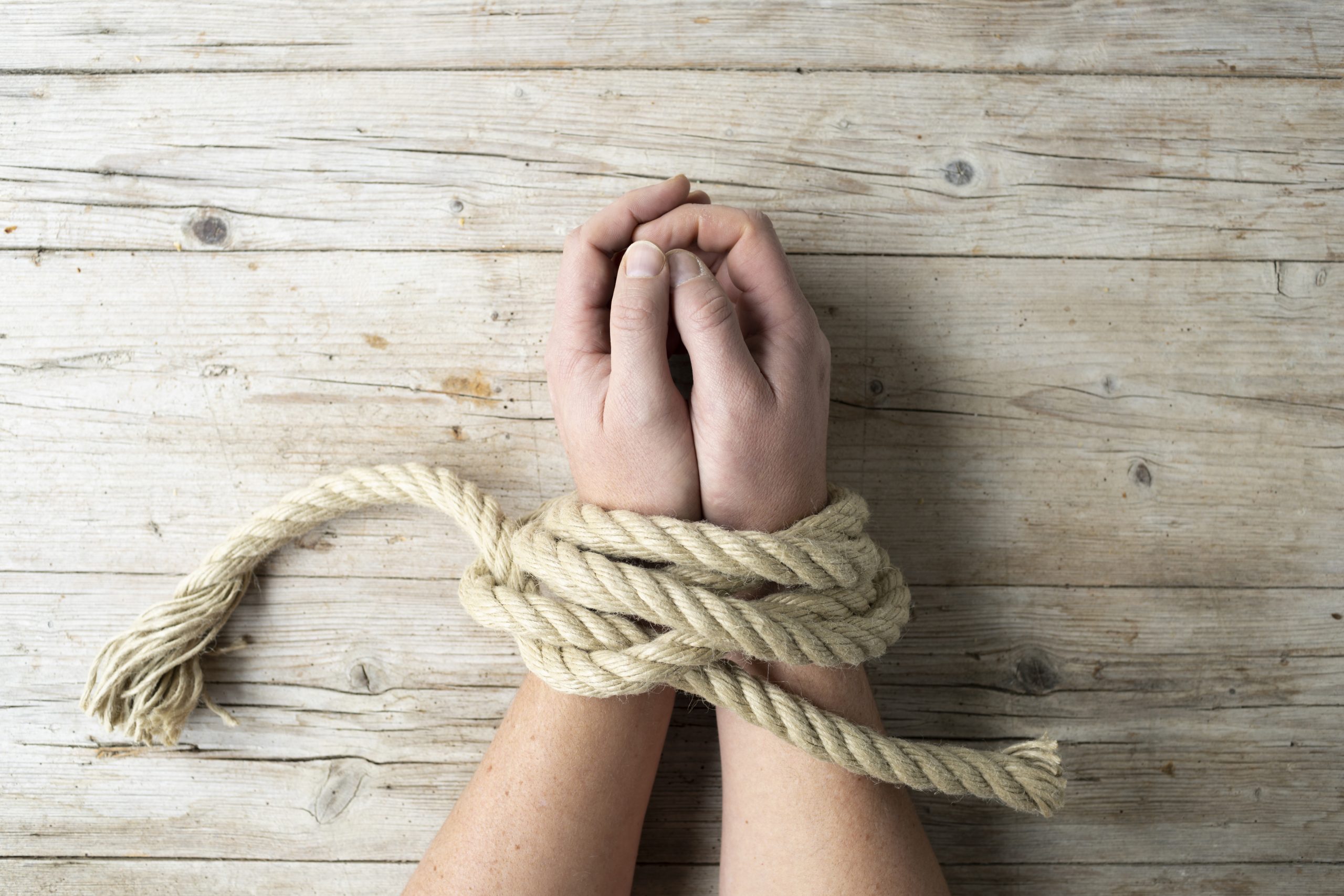 Hands of a man are tied and lie on light wooden background, addiction themed concept, photo taken from above Traumabinding